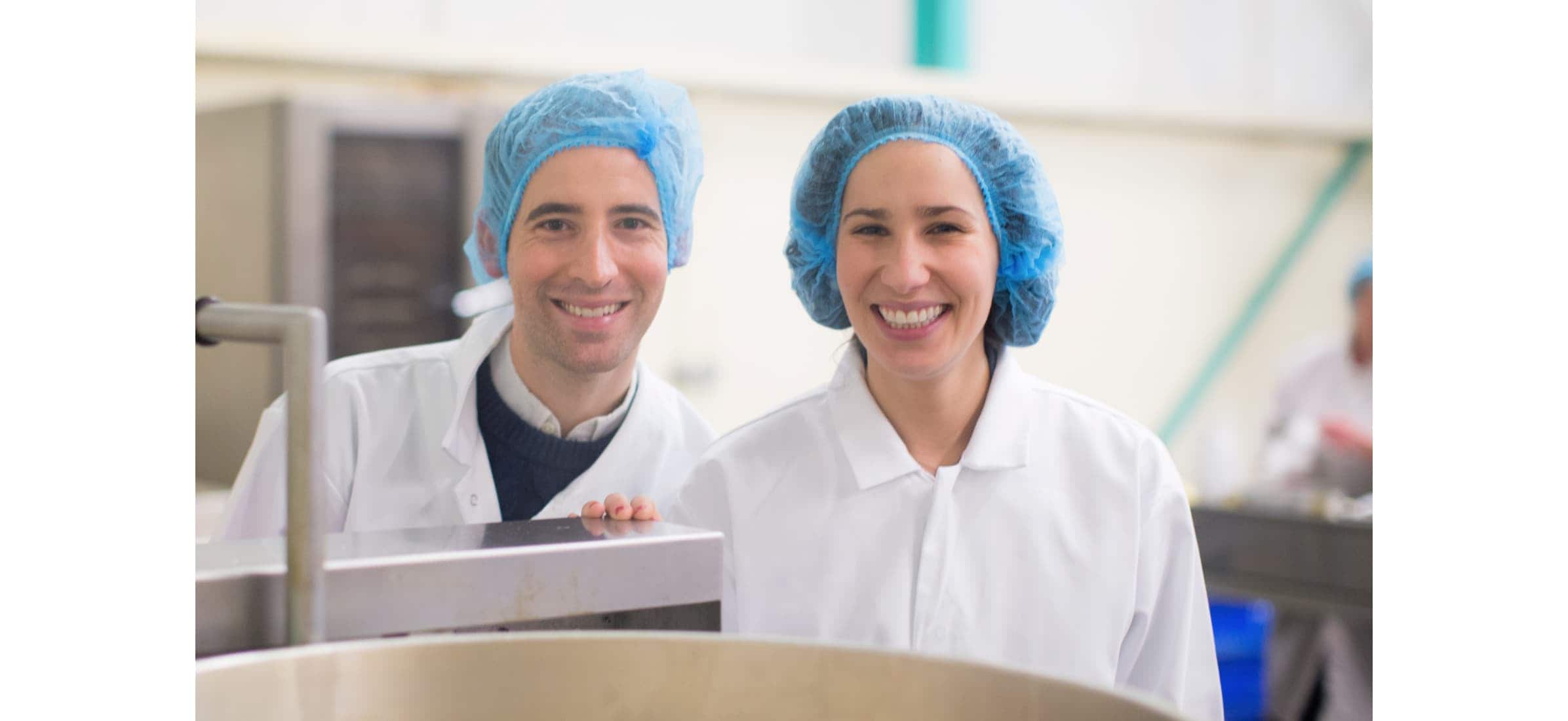 Co-founders of Popcorn Shed Laura Jackson and Sam Feller standing in an industrial kitchen wearing safety clothing.